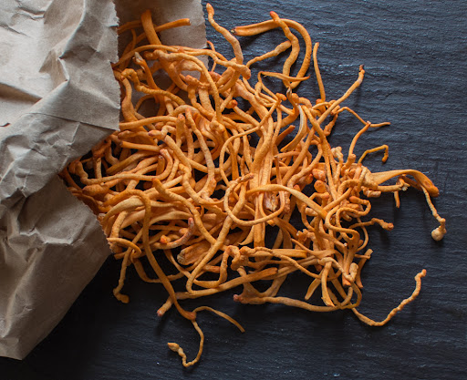 Dried Cordyceps mushrooms spilling from a paper bag onto a dark surface, known for their energy-boosting and stamina-enhancing properties.