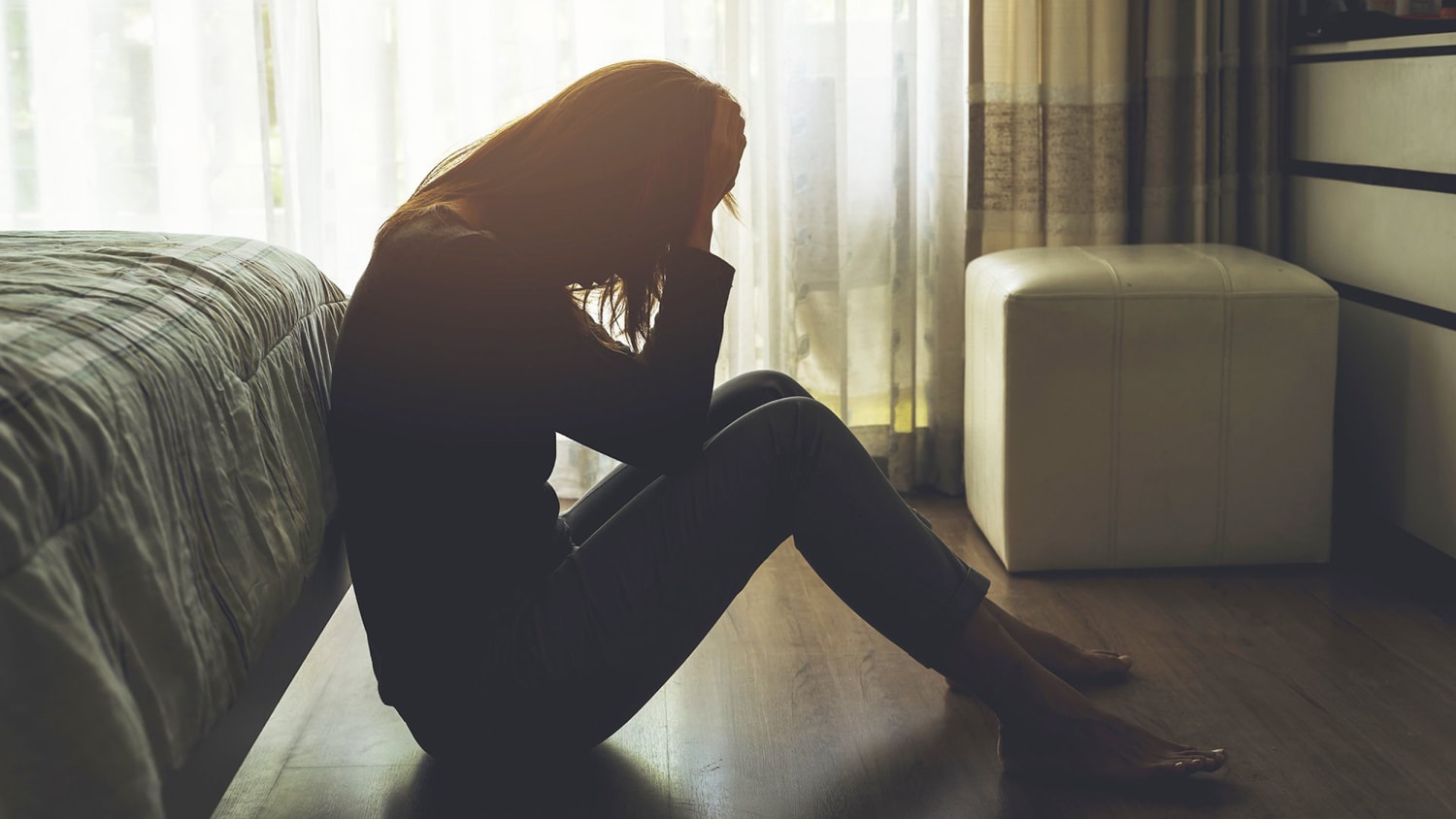 Silhouetted woman sitting on the floor with head in hands, representing depression and emotional distress.